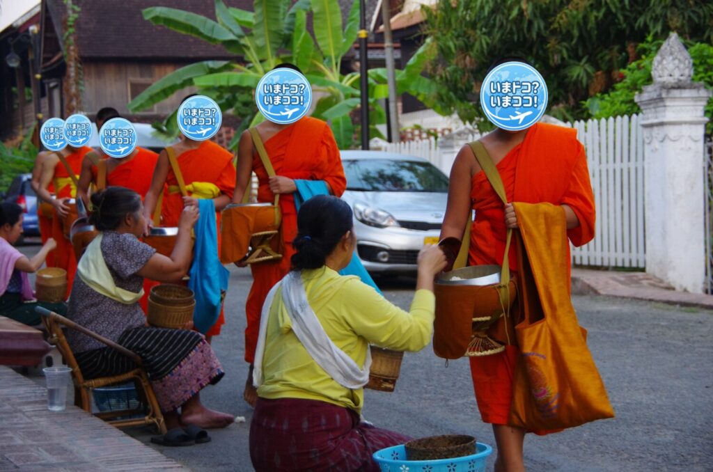 ラオスのルアンパバーンで、早朝の托鉢のときに一般の人たちが家の前を通る僧侶の鉢に食物を渡しているのを後ろから撮った写真