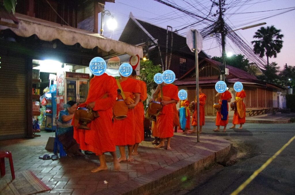 ラオスのルアンパバーンで、早朝の托鉢のときに一般の人たちが家の前を通る僧侶の鉢に食物を入れているのを撮った写真