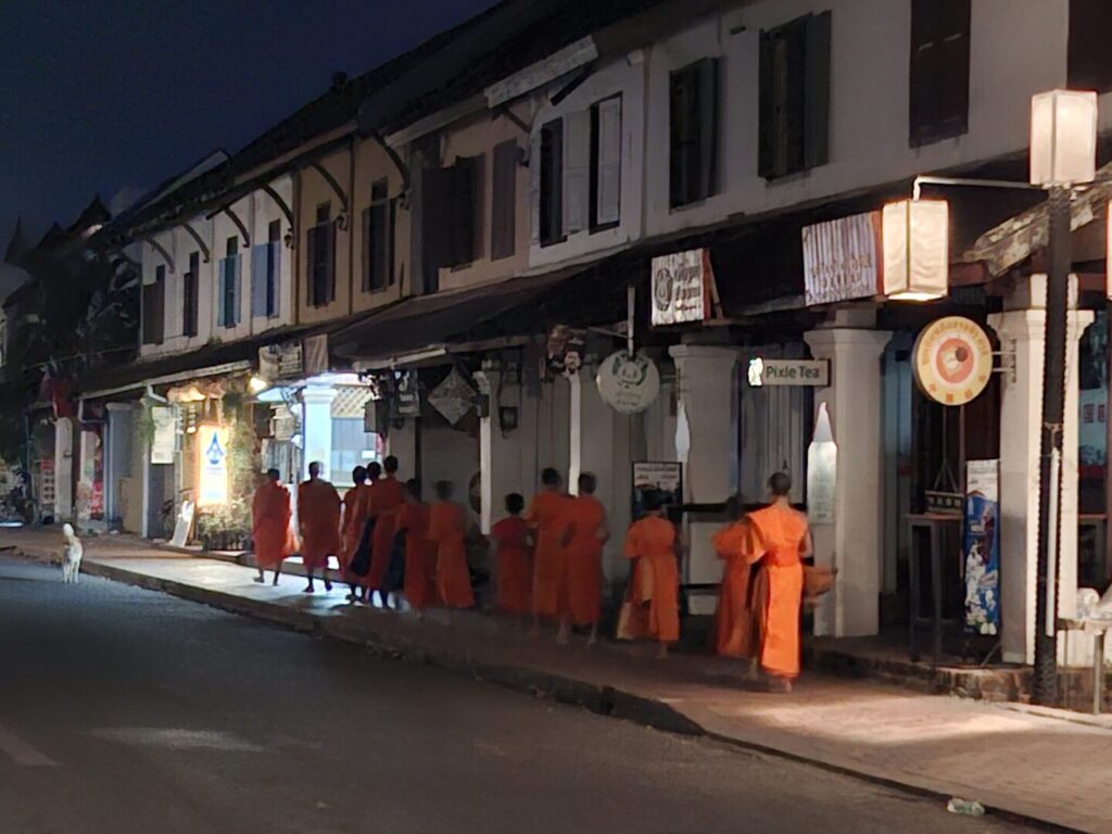 ラオスのルアンパバーンで、早朝の托鉢のために大勢の僧侶が寺院から出てきて道路を歩いているのを撮った写真