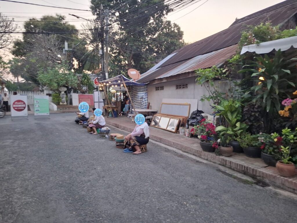 ラオスのルアンパバーンで、早朝の托鉢のときに一般の人たちが家の前を通る僧侶を待っているのを遠くから撮った写真