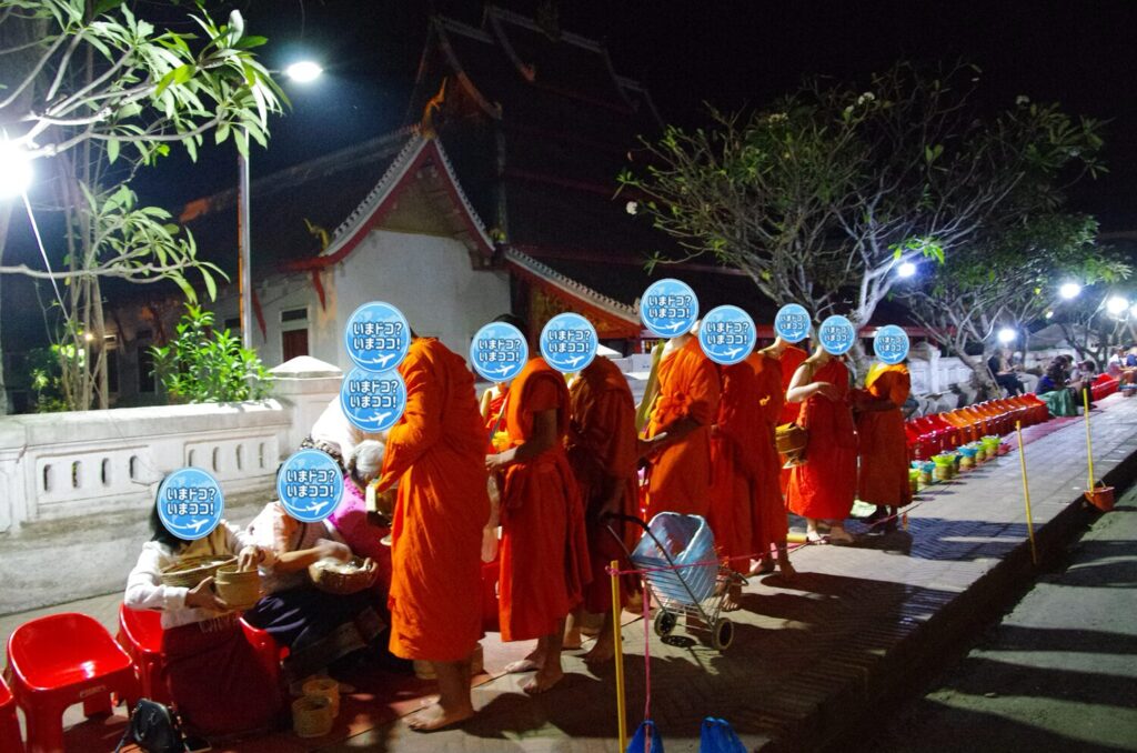 ラオスのルアンパバーンで、早朝の托鉢のために僧侶が寺院から出てきて、観光客が食物を鉢に入れているのを撮った写真