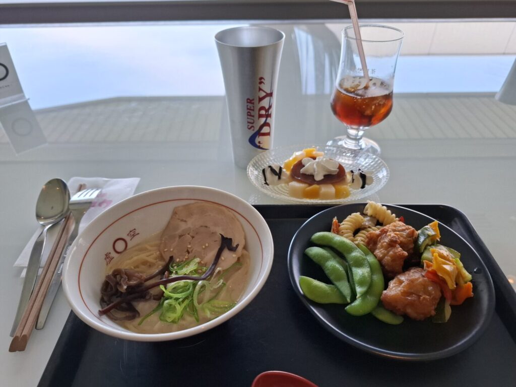 筆者が訪れた成田空港の第2ターミナルのラウンジKocooで提供されるラーメンや唐揚げと、プリンアラモードなどをとった写真