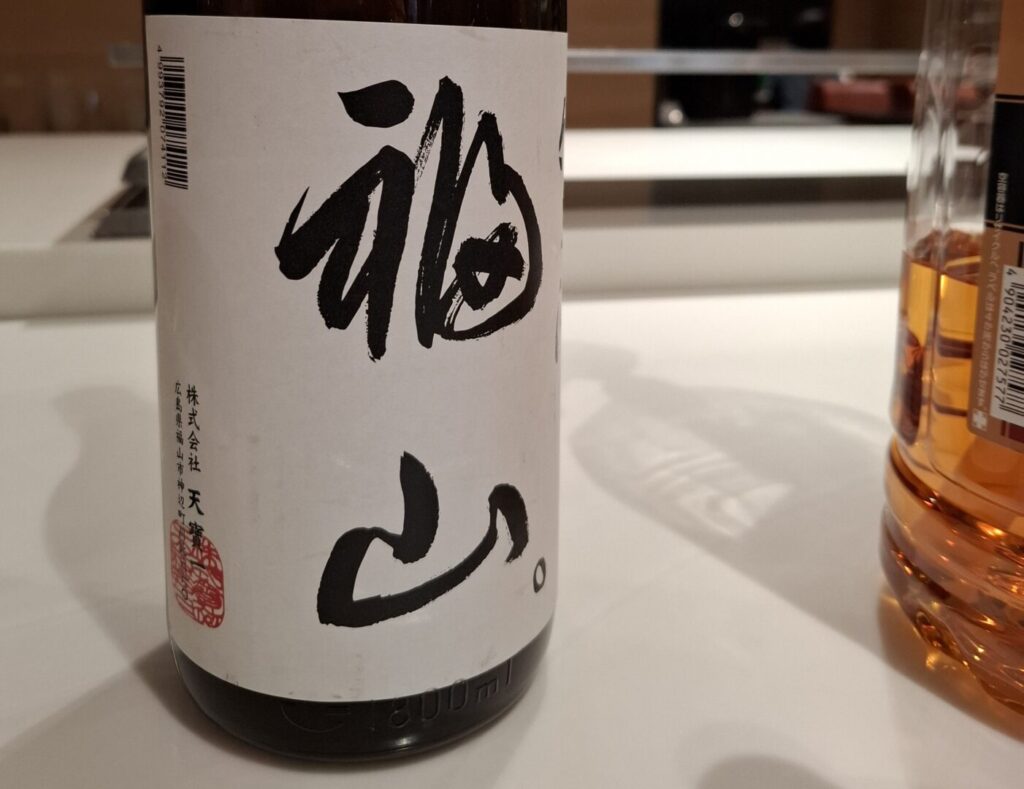 筆者が訪れた広島県福山市で宿泊したカンデオホテルズ福山でハッピーアワーで提供された日本酒の純米酒福山のラベルをアップで撮った写真