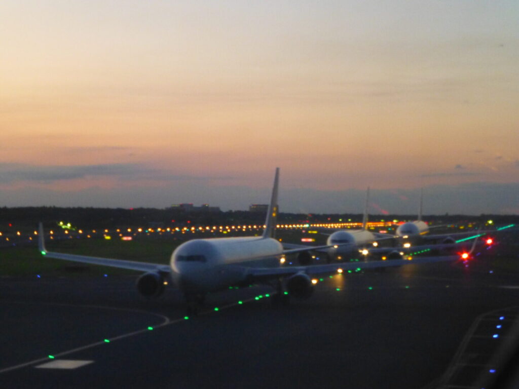 筆者が日本からタイに行く飛行機の中で撮影した、夕暮れをバックに出発待ちの航空機の列を撮った写真