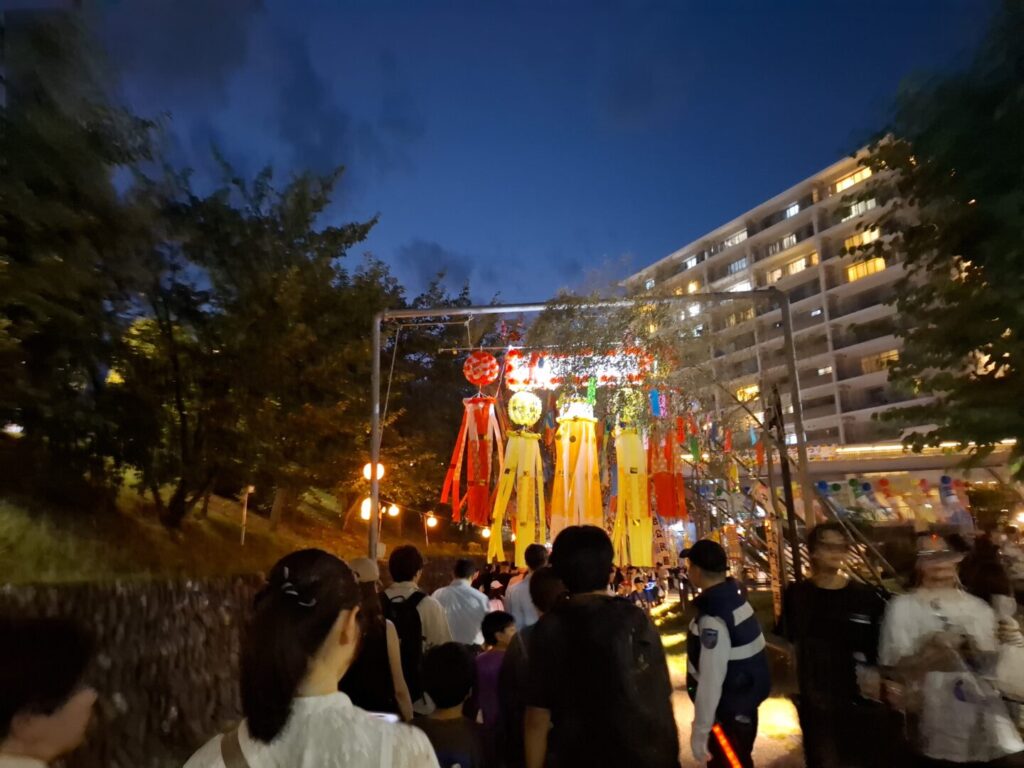 筆者が訪れた狭山市入間川七夕まつりで夕暮れ時に提灯などに明かりが灯り始めたころの様子を撮った写真